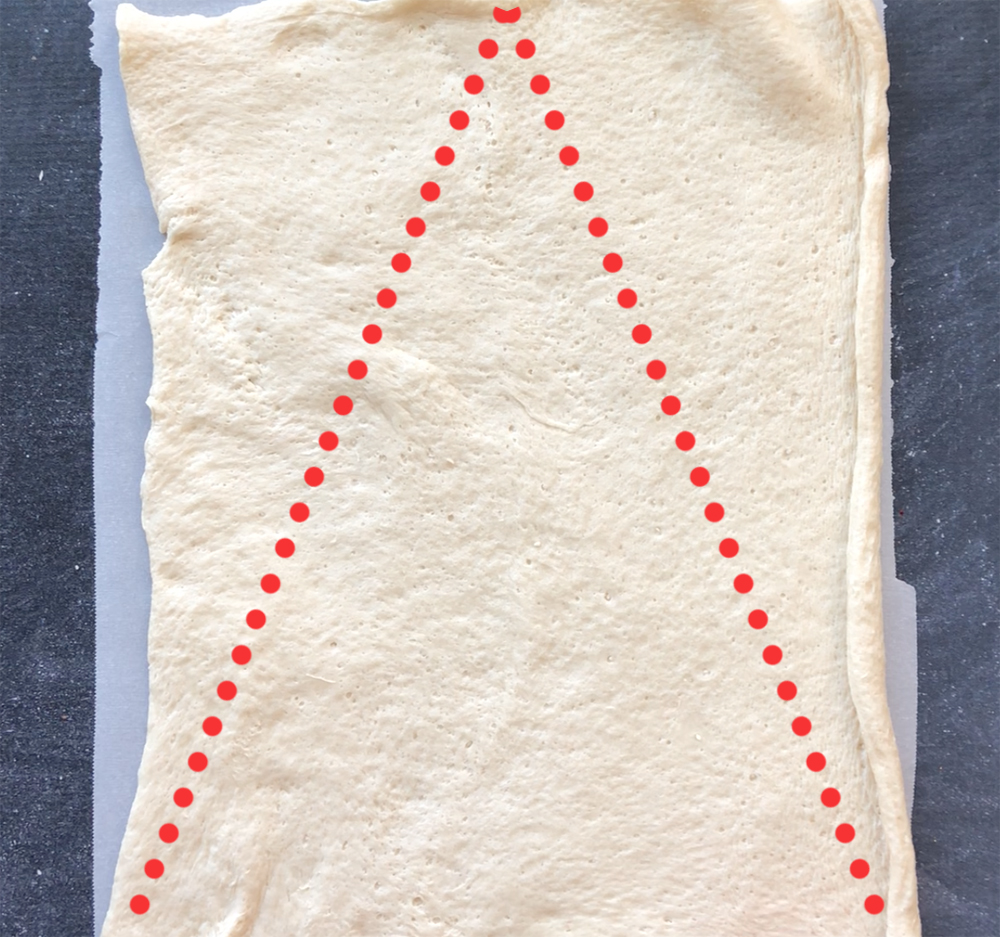 Refrigerated pizza dough unrolled on parchment paper with triangle marked on it
