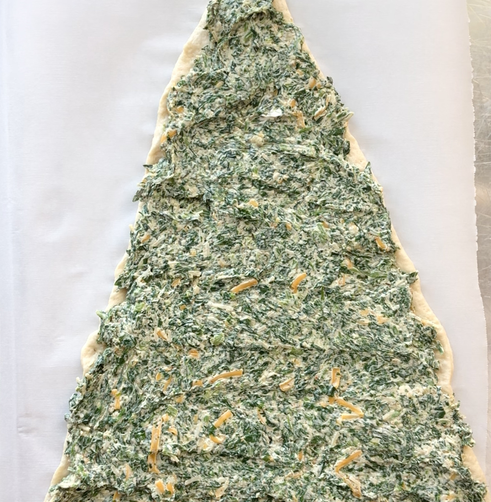 Triangle of pizza dough covered with spinach dip