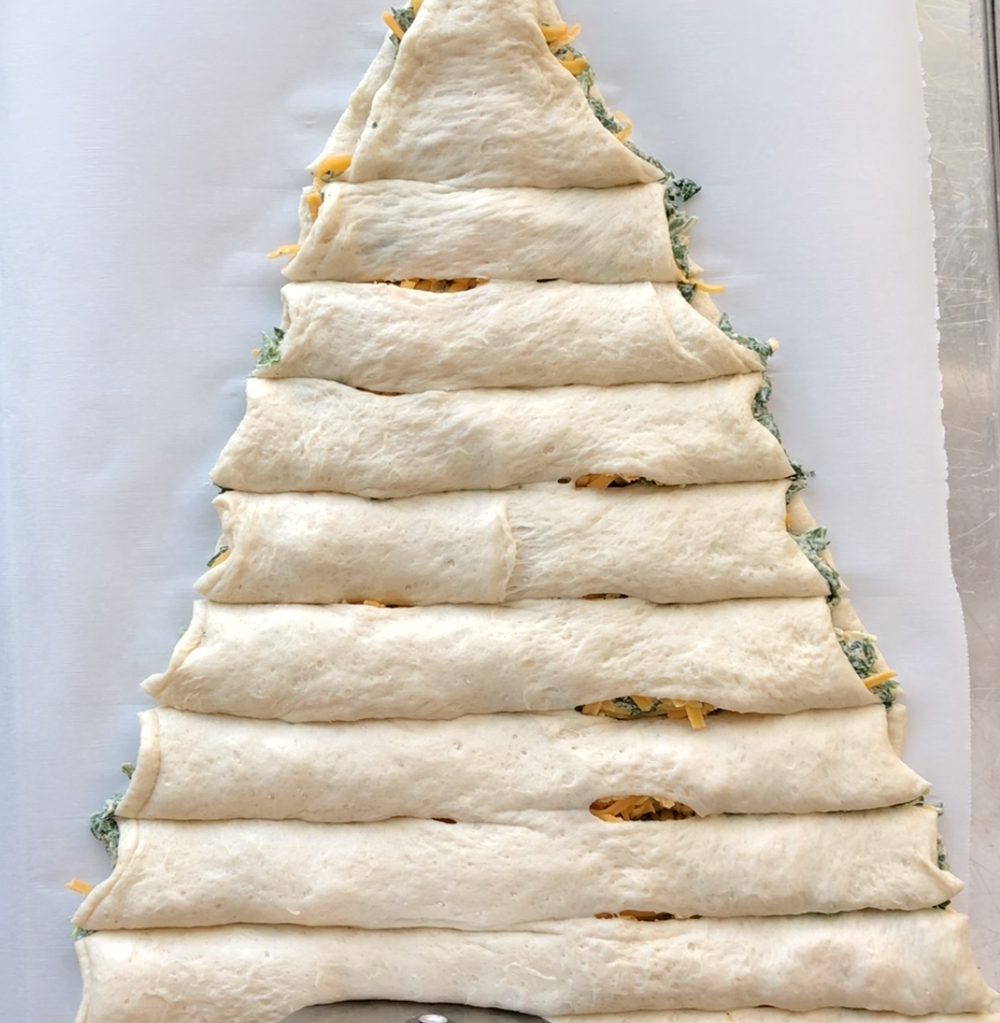 Spinach dip in between two triangle of pizza dough, with slices cut horizontally from near the center to left and right sides