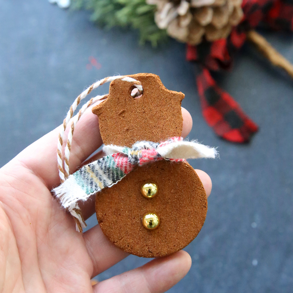 Hand holding a cinnamon Christmas ornament in the shape of a snowman