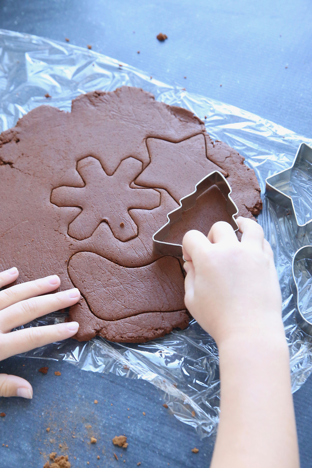 Hand using cookies cutters to cut Christmas shapes from cinnamon applesauce dough