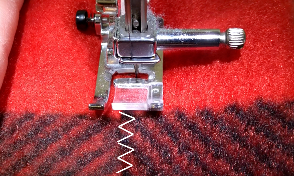 A close up of a sewing machine making a zigzag stitch on the folded portion of fleece