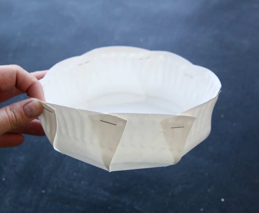 Hand holding paper plate that has been cut and sides folded up and stapled to make a basket