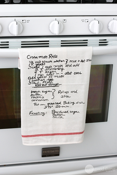 Kitchen towel with cinnamon roll recipe on it hanging on an oven door