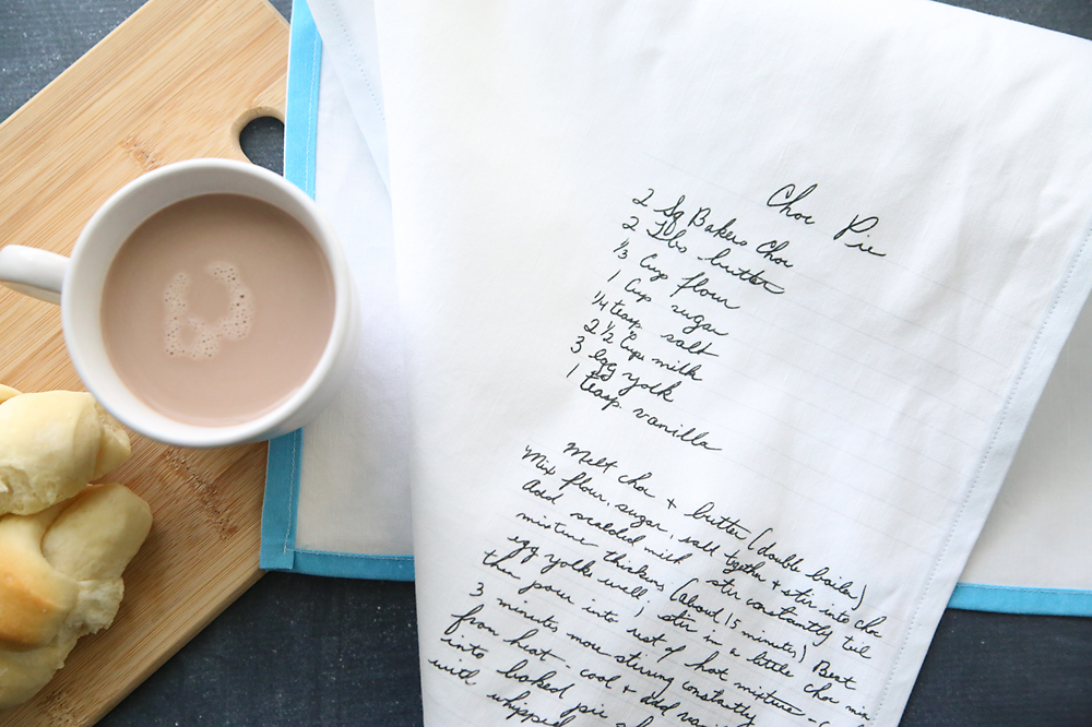 Grandma\'s handwritten recipe transferred onto a tea towel, sitting with a cup of cocoa