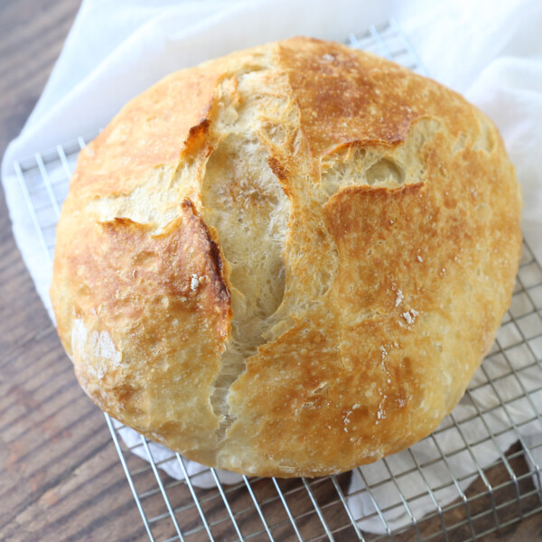 Loaf of artisan bread on a cooling rack with kitchen towel