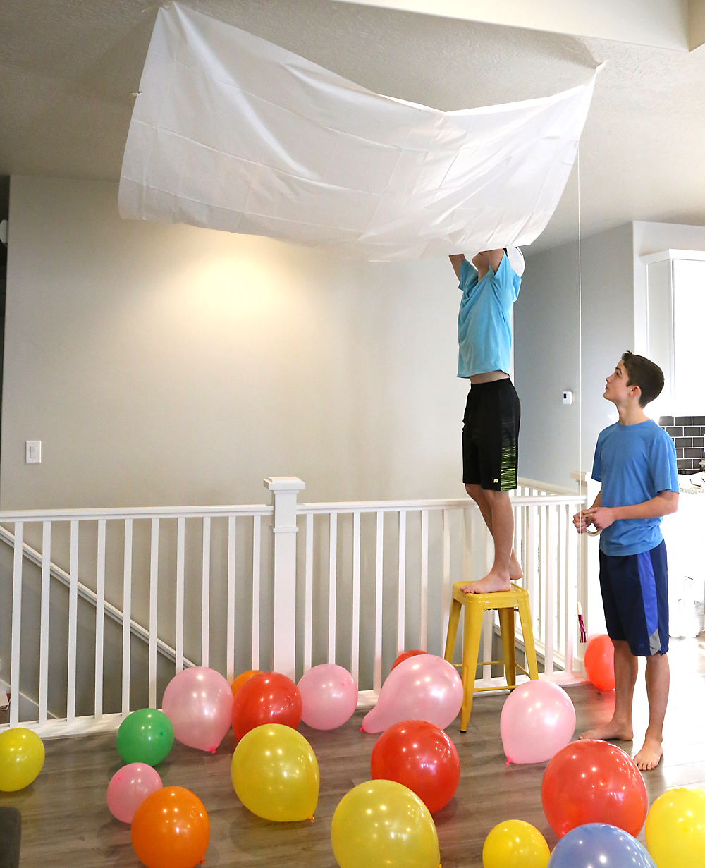 Boys taping a tarp to the ceiling to fill with balloons