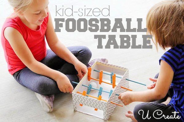 Two kids playing with a DIY foosball toy made from a cardboard box