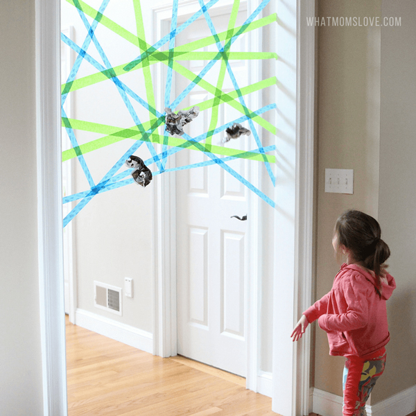 A little girl throwing paper to spiderweb made from masking tape across a doorway