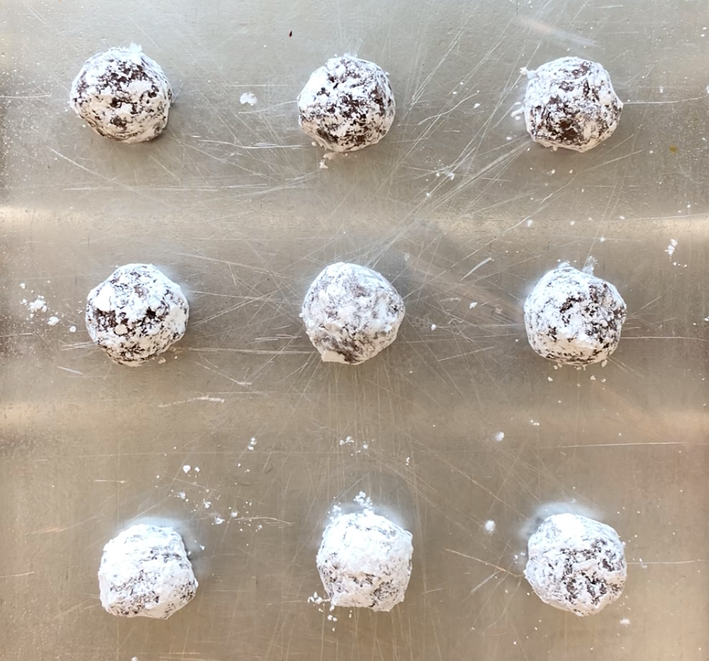 Chocolate cookie dough balls covered in powdered sugar on a cookie sheet