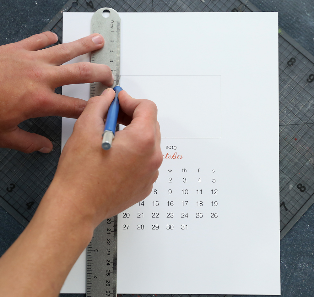 Hand using exacto knife and ruler to cut photo window out of calendar template