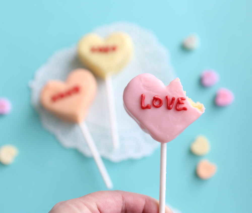 Cake pops decorated to look like conversation hearts with words written on them