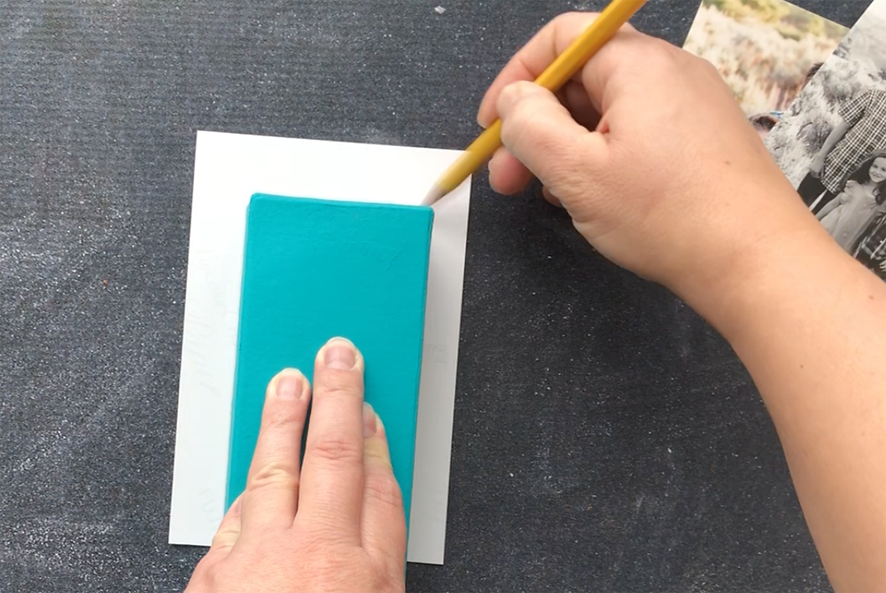 Hand using a pencil to trace around the edge of a paper mache letter on the back of a photo