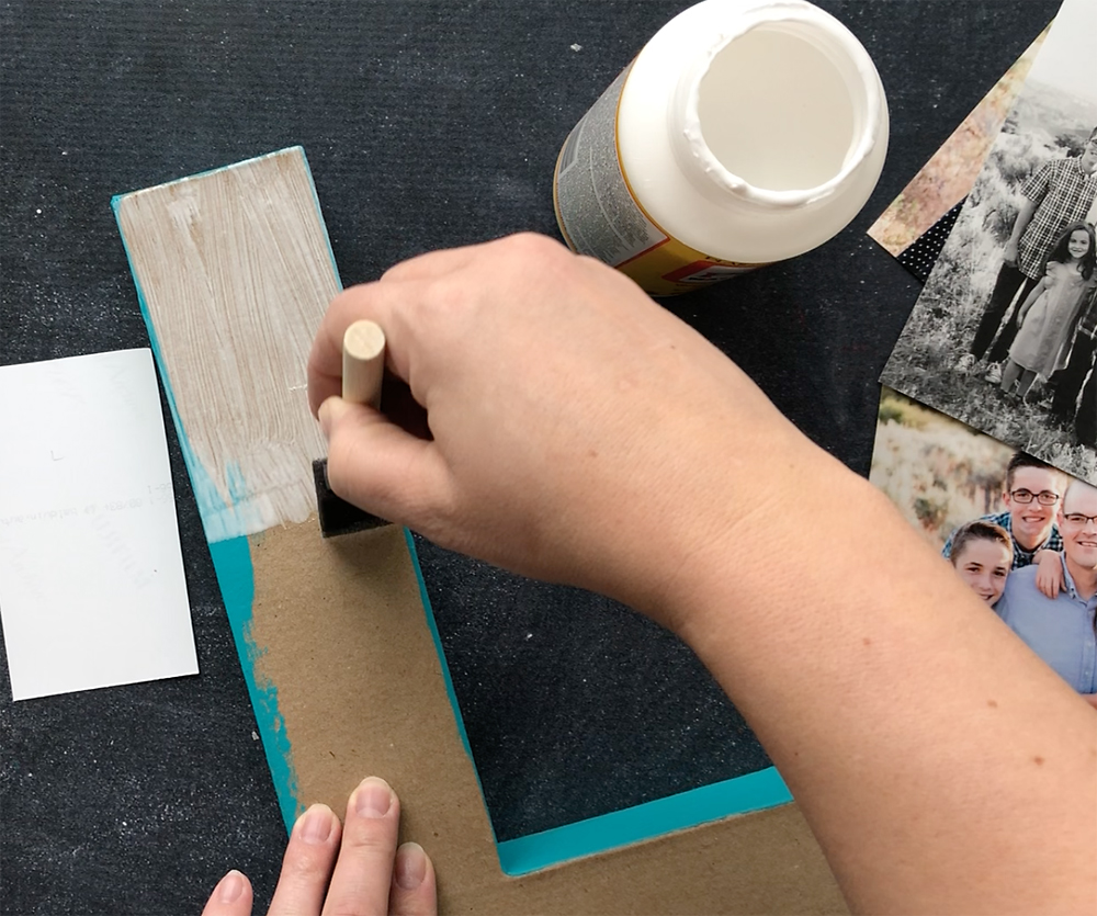 Hand using a small foam paintbrush to spread Mod Podge on the paper mache letter