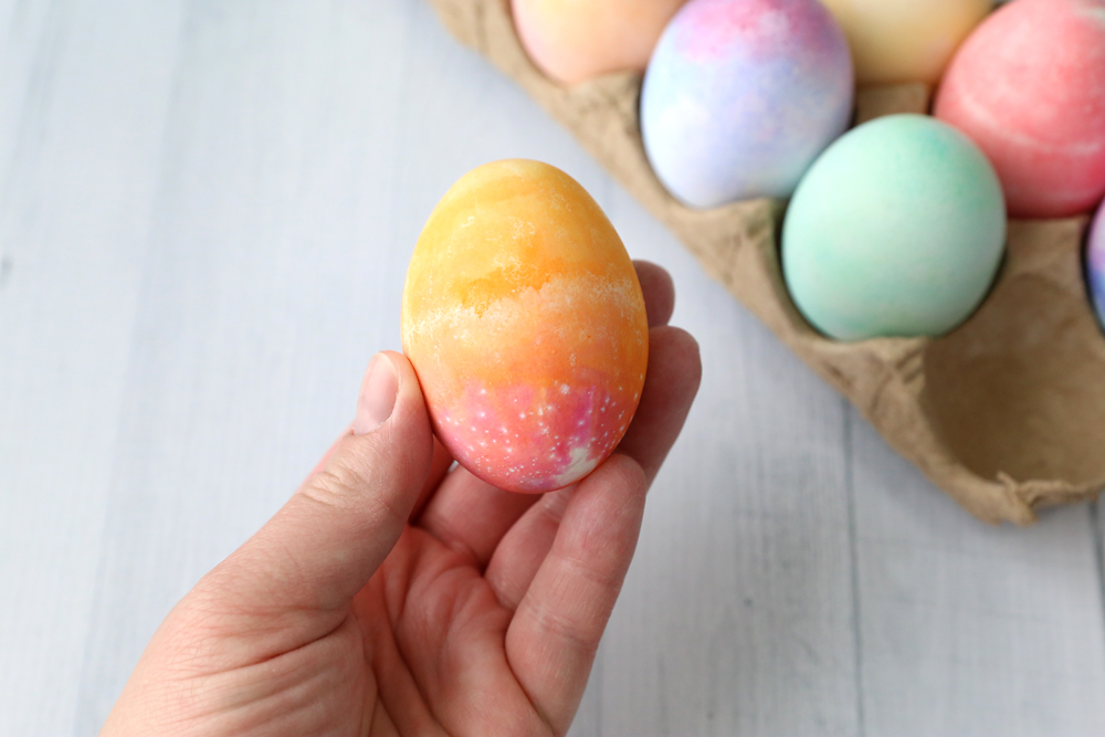 Hand holding colored Easter eggs that is yellow on top and red on the bottom
