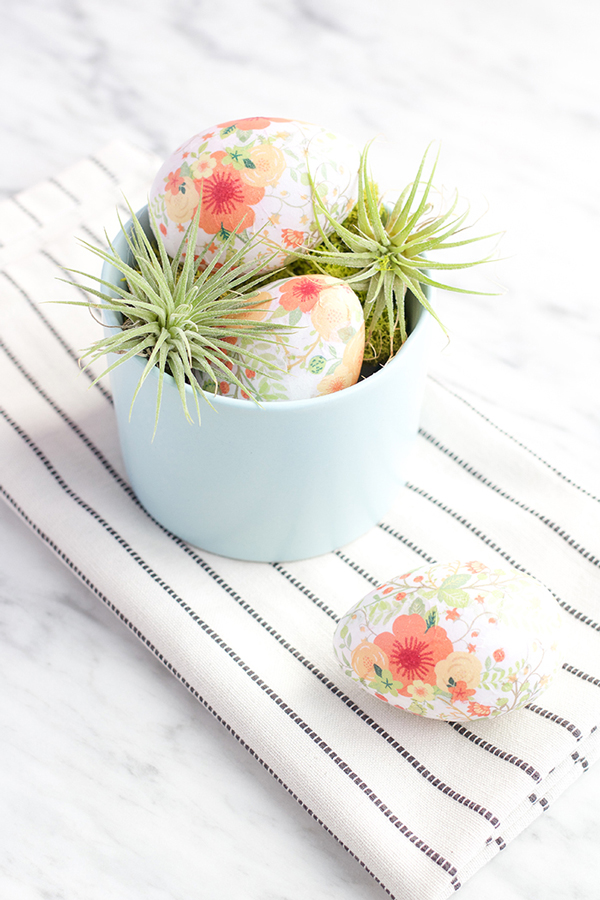 Easter eggs decorated with pretty floral designs in a bowl with greenery