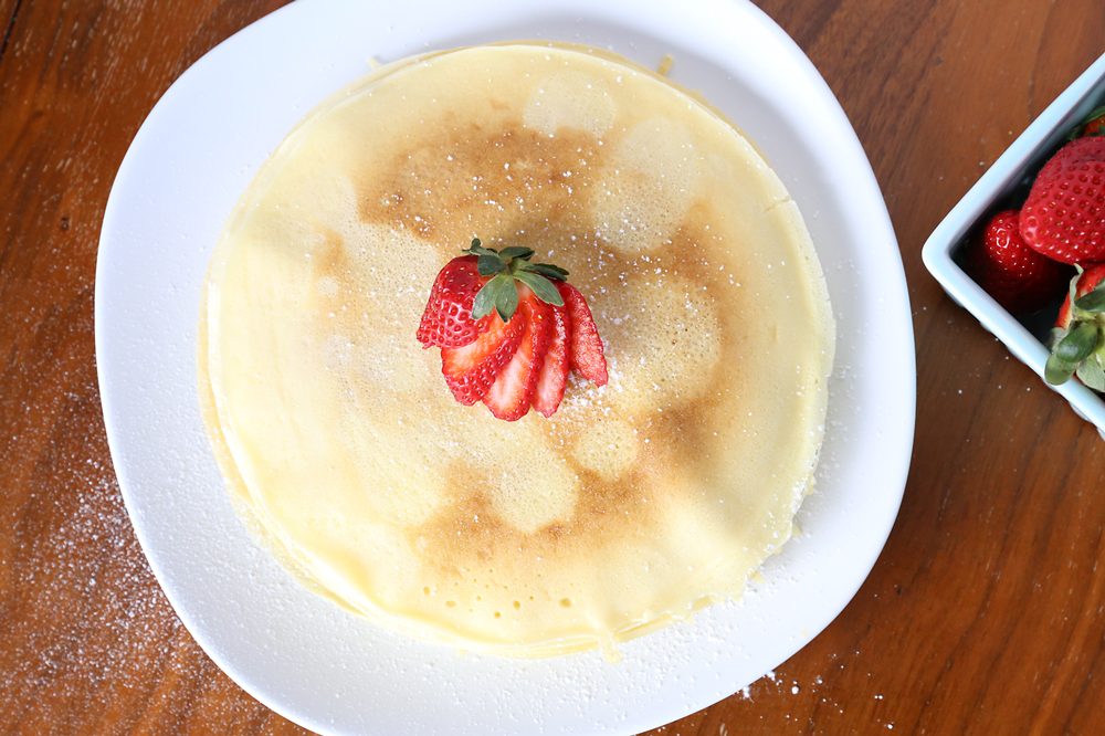 Perfectly round homemade crepes on a plate with a strawberry on top