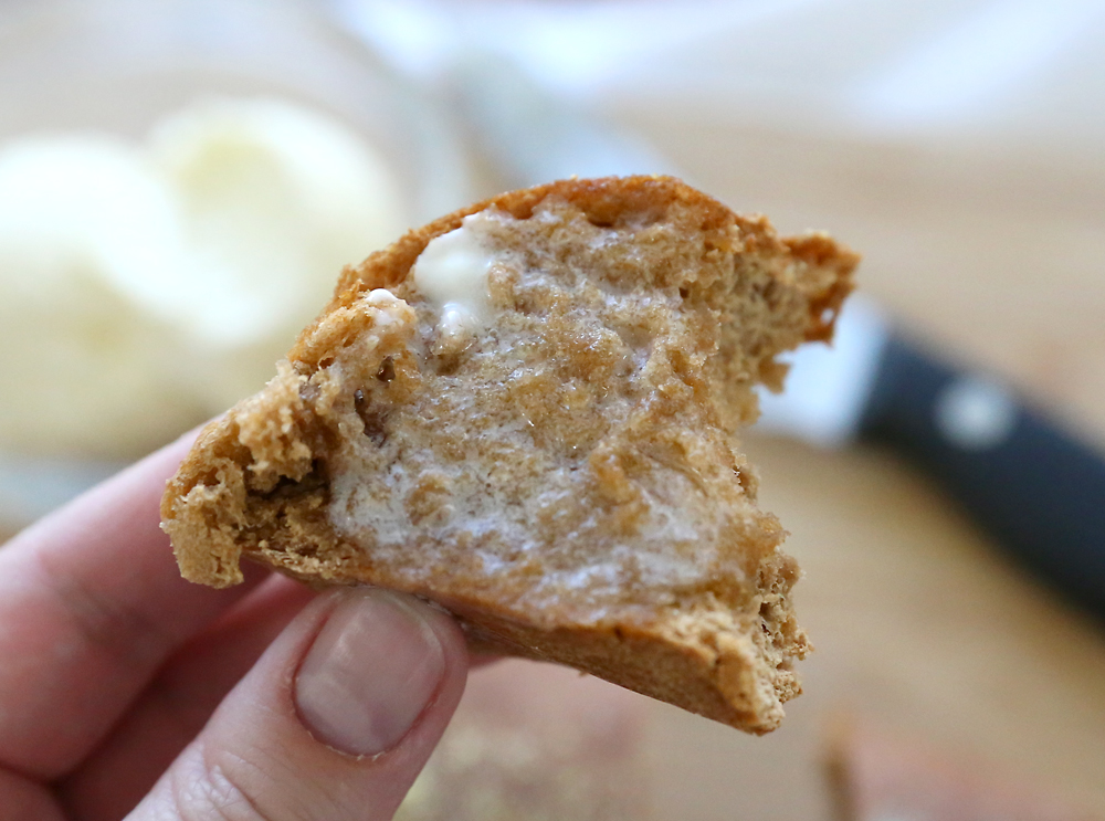 Hand holding half eaten piece of brown bread smothered in butter