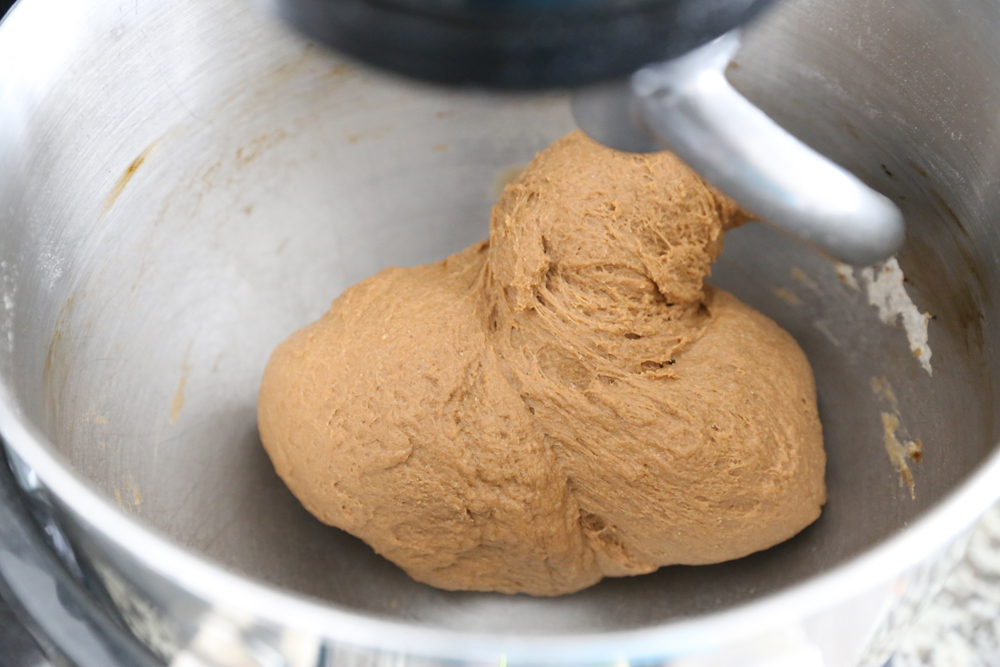 Brown bread dough in a mixer bowl pulling away from the sides