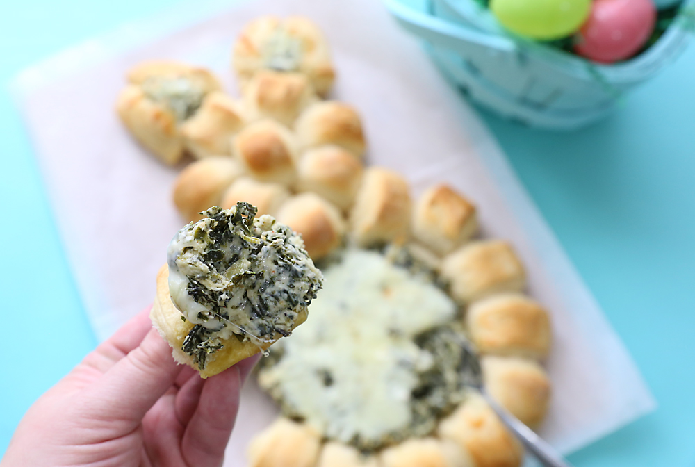 Handing holding a small bread roll covered in spinach dip