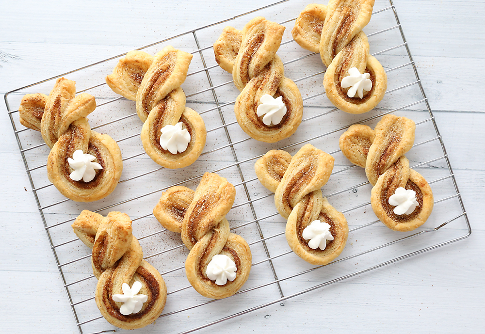 Cinnamon sugar bunny treats made from twisted strips of puff pastry with dots of whipped cream for tails