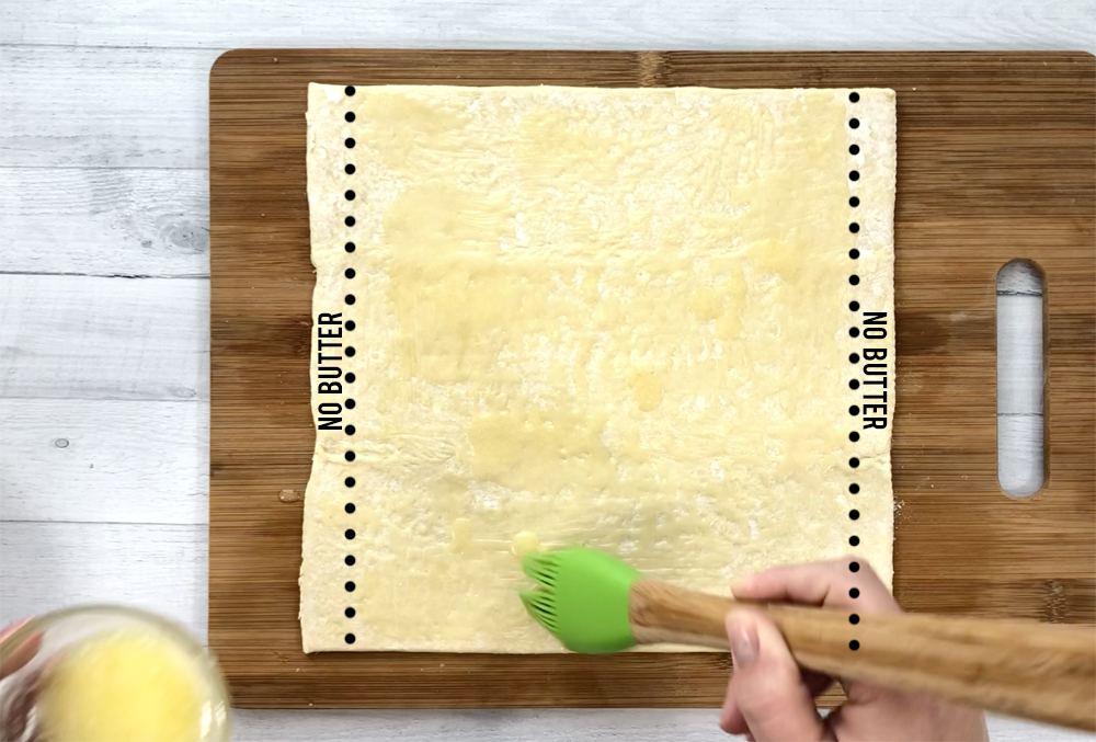 Hand brushing butter over a puff pastry sheet
