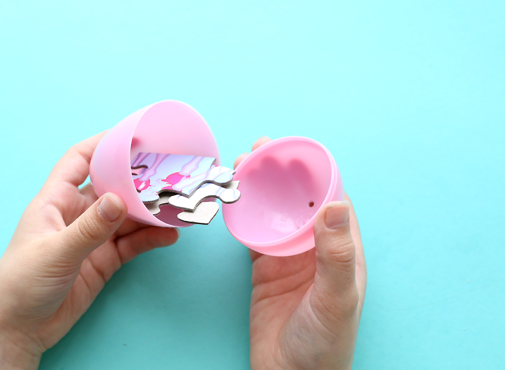 Hands opening plastic Easter egg with puzzle pieces inside