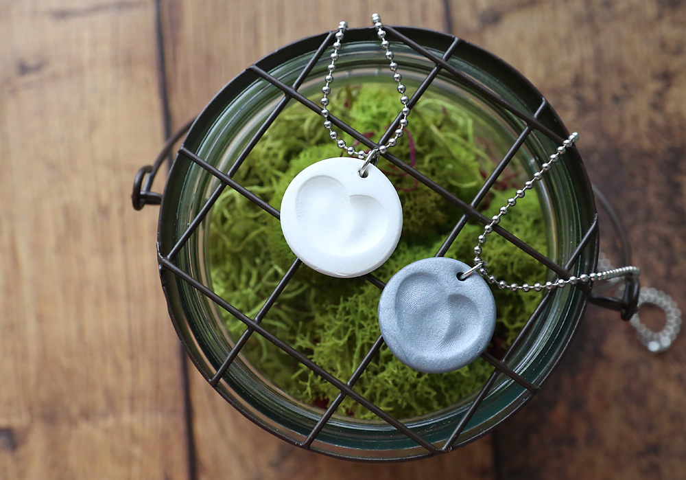 Small clay circles with fingerprints that form a heart made into necklaces