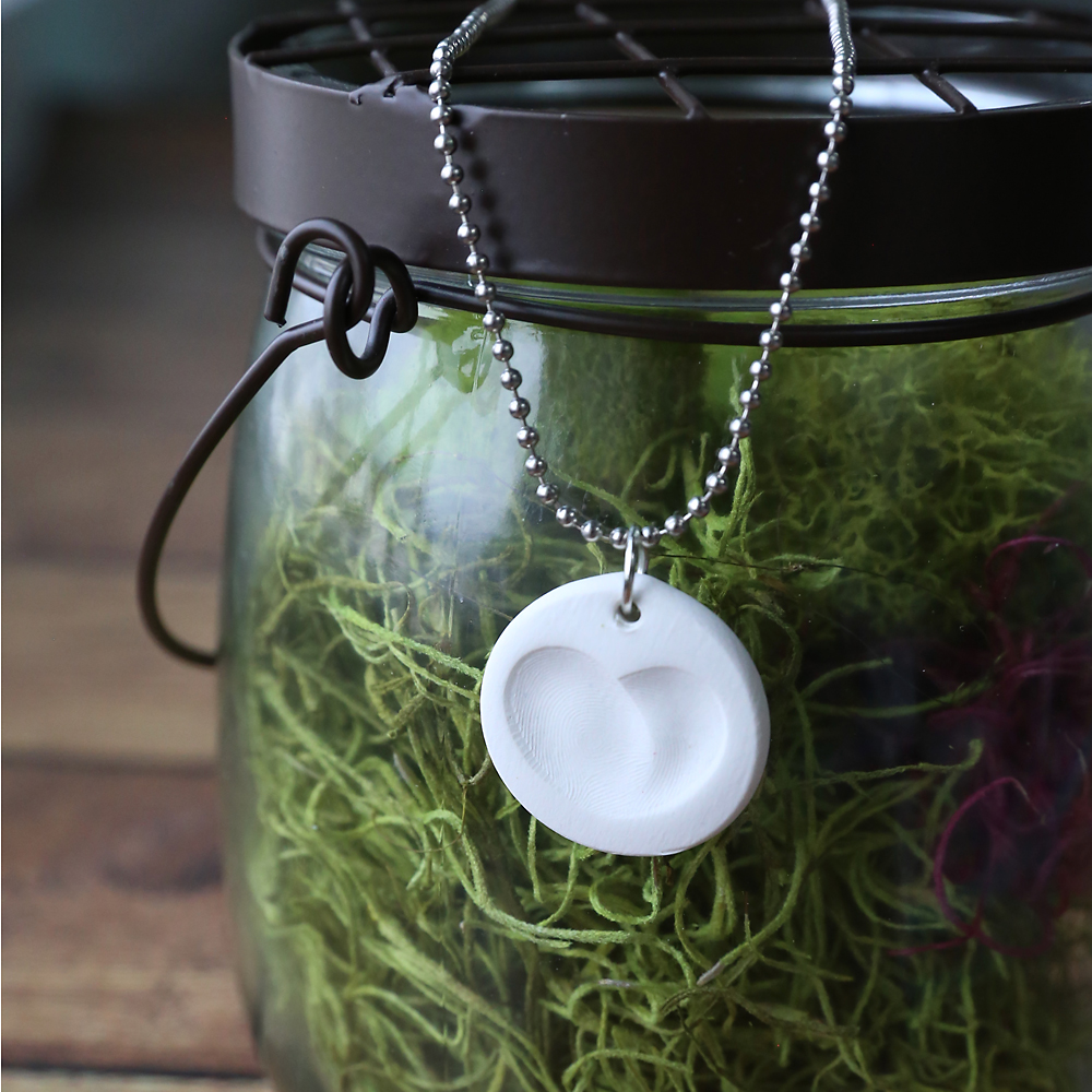 Small clay circles with fingerprints that form a heart made into necklaces