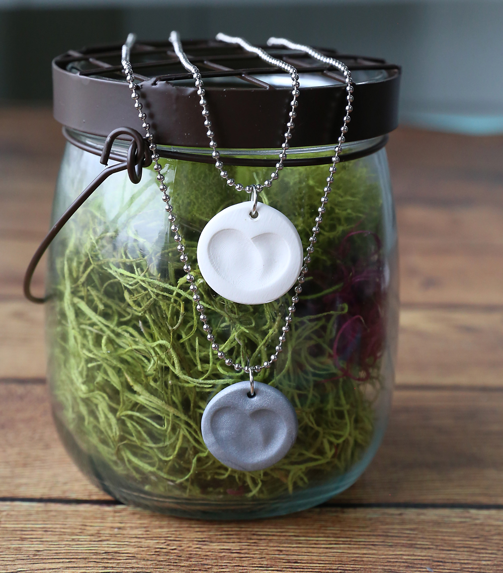 Small clay circles with fingerprints that form a heart made into necklaces