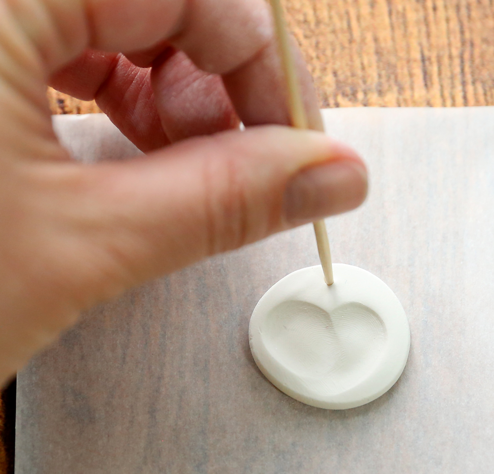 Using a toothpick to poke a hole at the top of the clay disc