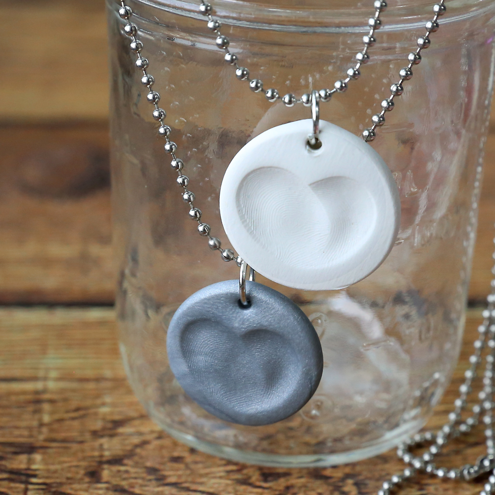 Small clay circles with fingerprints that form a heart made into necklaces