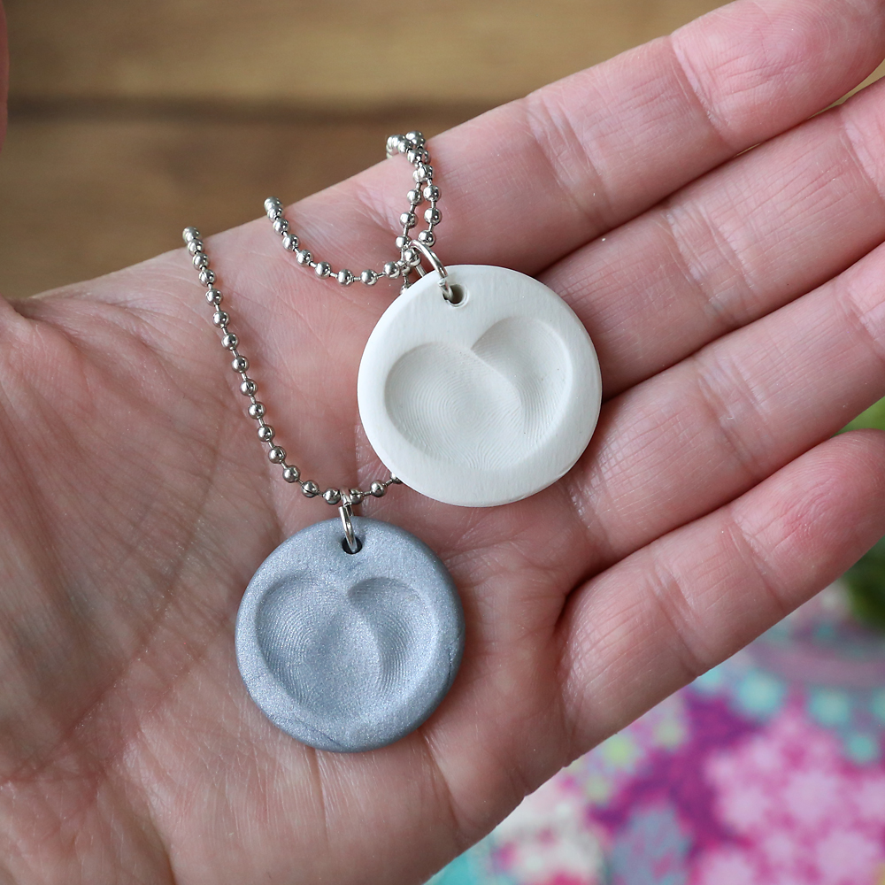 Hand holding fingerprint heart clay necklaces