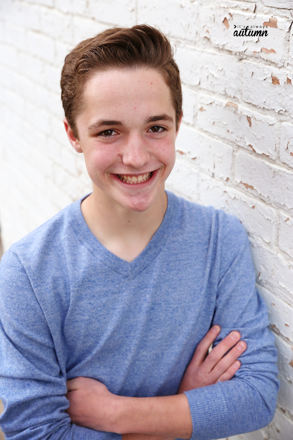 Poses for boys: a boy crossing his arms, leaning sideways against a brick wall