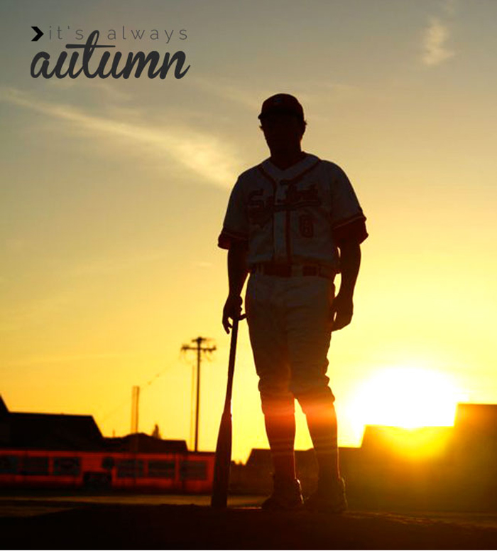 A silhouette of a boy with a baseball bat standing in a baseball field at sunset