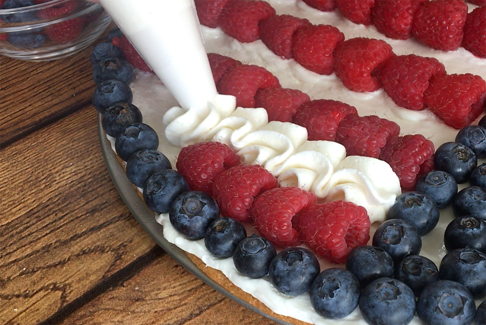 A piping bag that\'s piping cream for the white strips in the flag fruit pizza