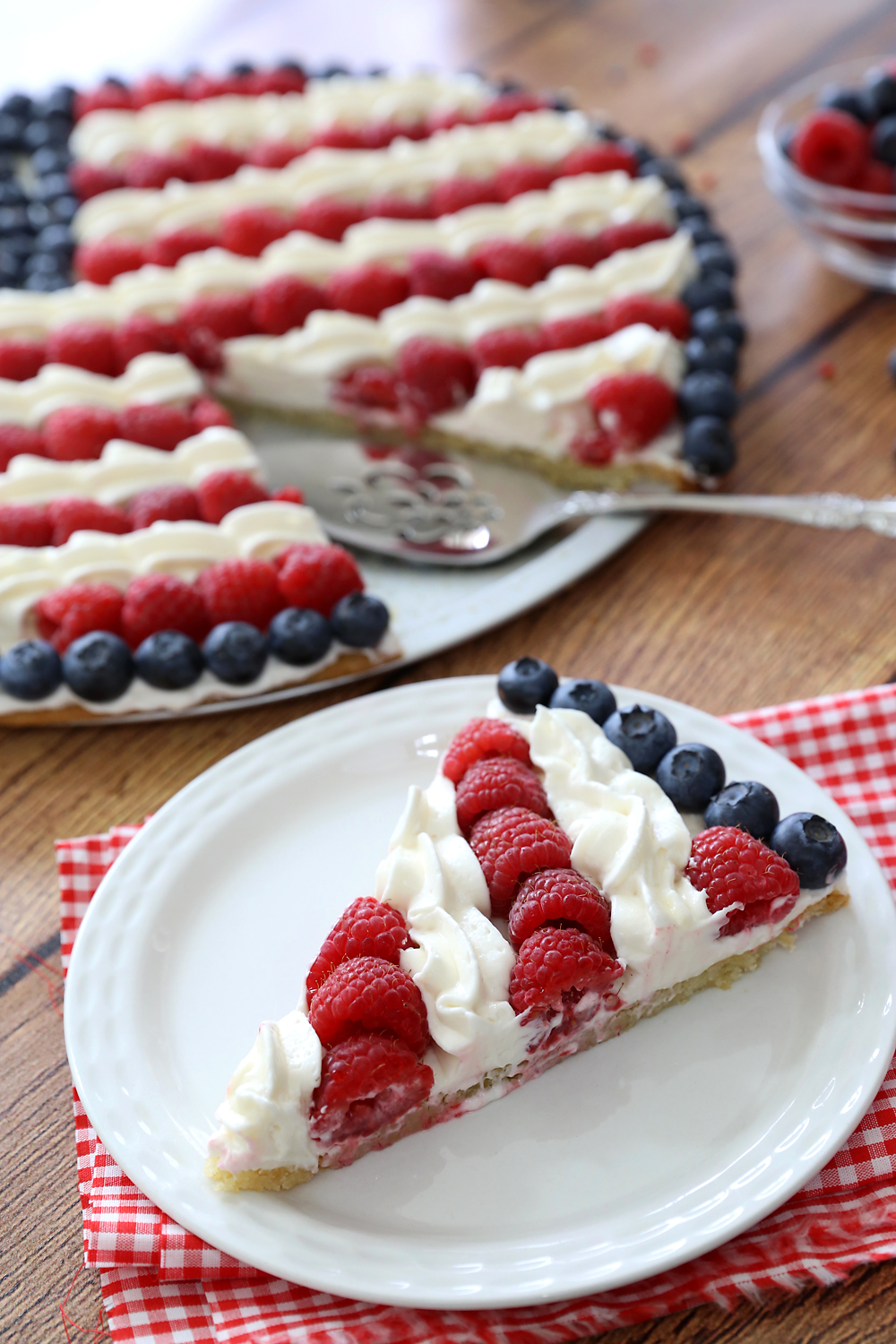 A slice of fruit pizza decorated with raspberries, blueberries, and cream to look like an American flag