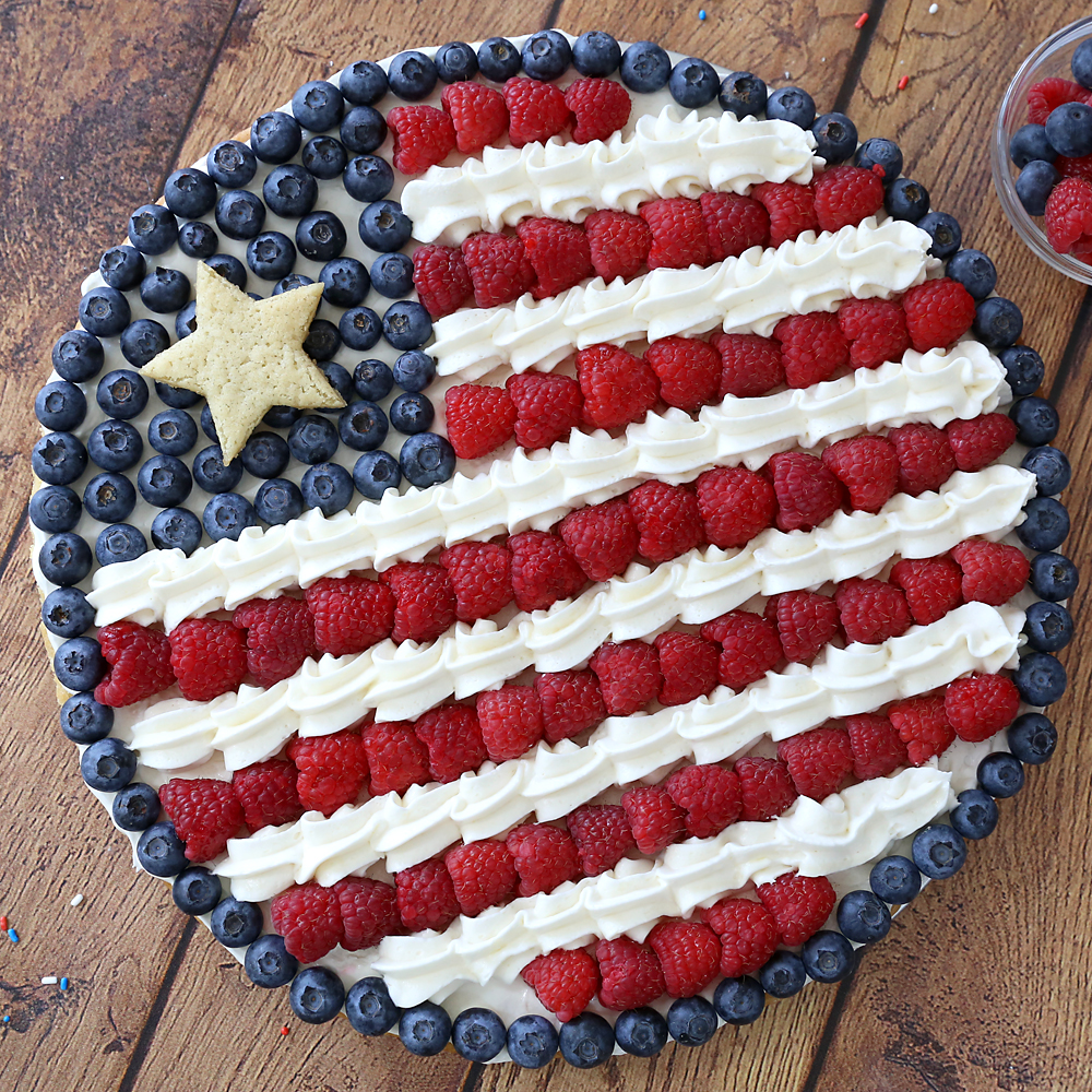 A large fruit pizza in the shape of an American flag, decorated with berries and cream