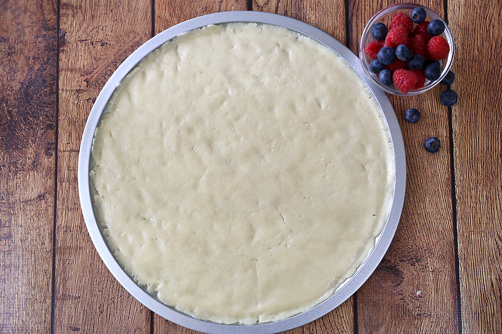 A pizza pan with sugar cookie dough pressed into it