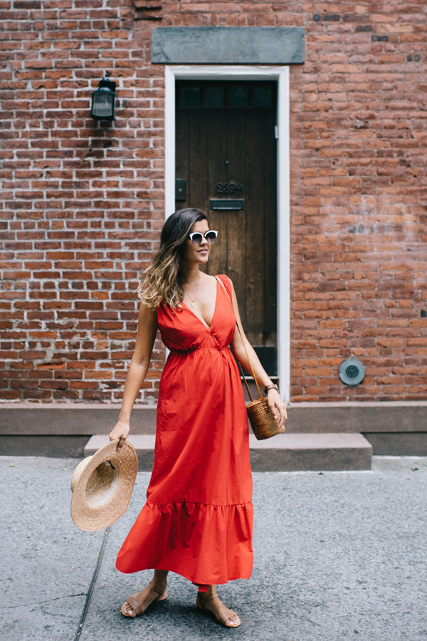 A woman wearing a sleeveless red maxi dress with ruffle at the hem