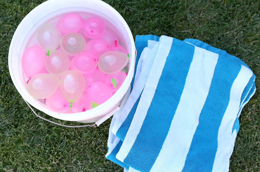 Water balloons in a bucket next to a folded beach towel