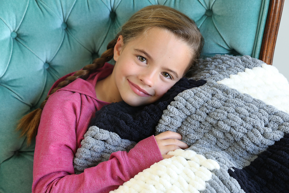 A little girl snuggling with a plaid loop yarn blanket