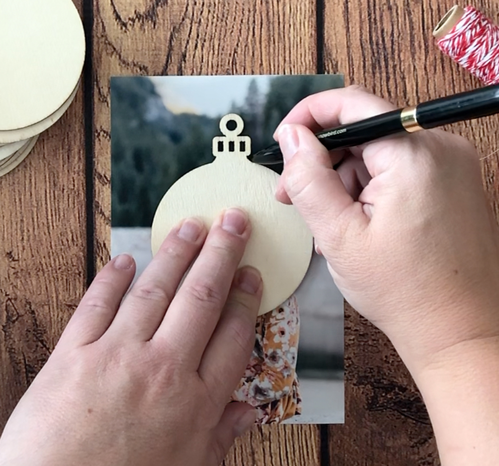 Unfinished wood ornament placed over photo, hands tracing around it