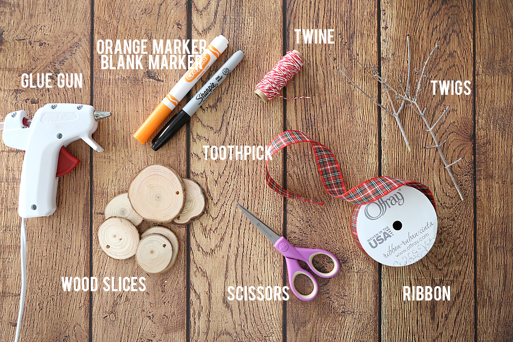 Snowman ornament supplies: orange and black markers, twine, sticks, toothpick, ribbon, wood slices, scissors, glue gun
