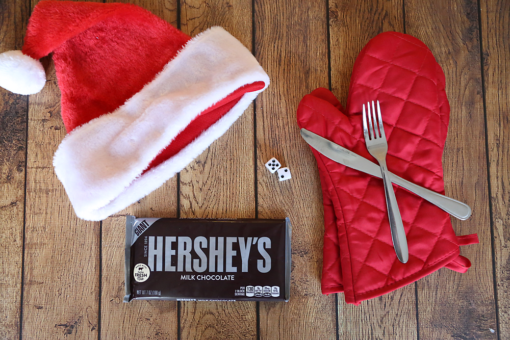 Supplies for candy bar game: Santa hat, dice, oven mitts, fork and butter knife, large chocolate bar