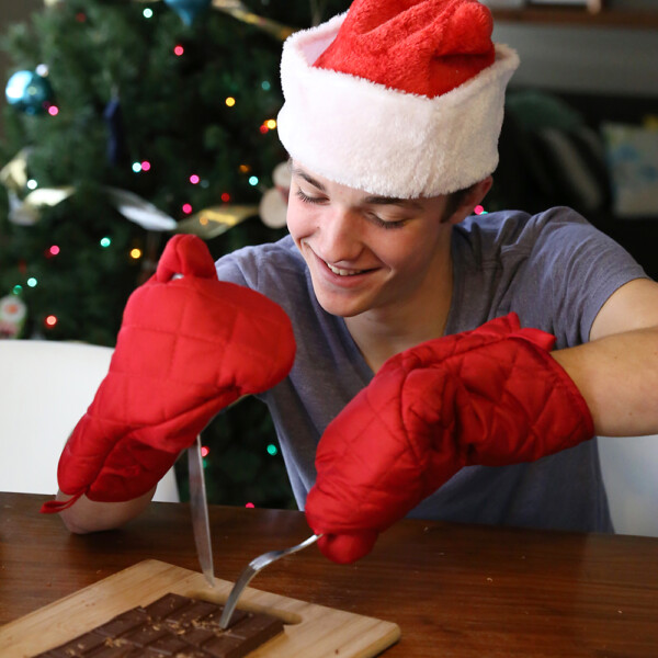 Boy in Santa hat and oven mitts cutting chocolate bar with a fork and knife