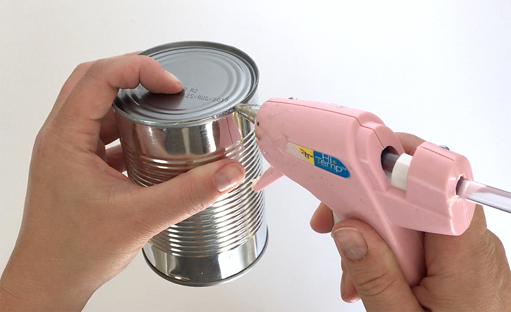 Hands gluing the bottom of the can back on with hot glue