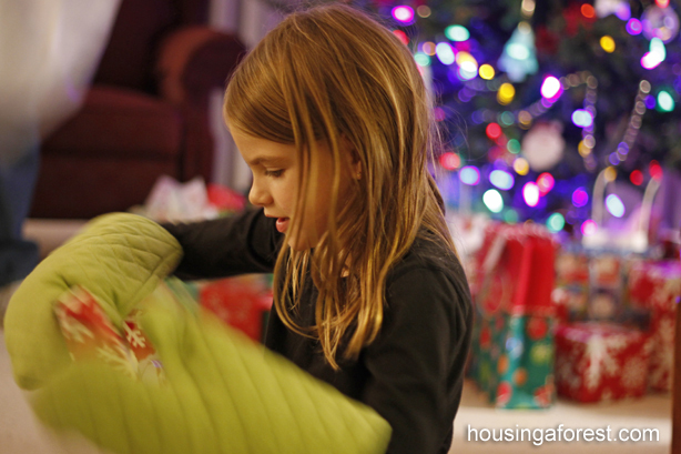 Girl trying to unwrap gift while wearing oven mitts