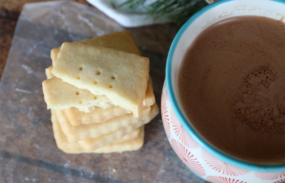 Stack of shortbread cookies on a table next to a cup of cocoa