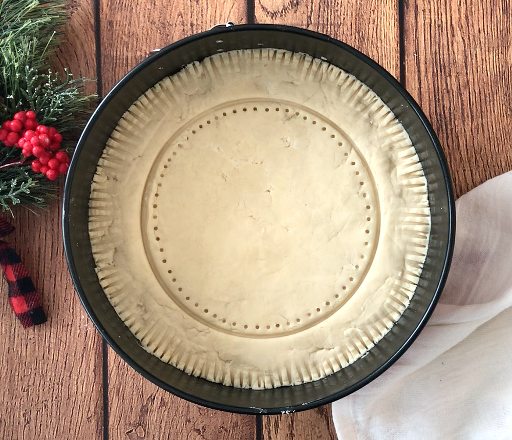 Shortbread dough in a springform pan decorated with fork tines, circle, and dots
